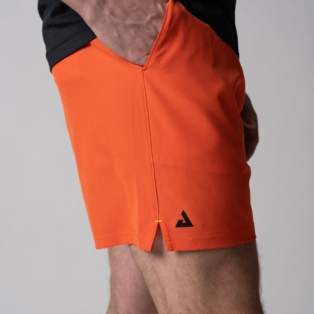 Gray background, close up of a black JOOLA trinity logo on the right leg of a pair of Men's Woven Short, poppy red.