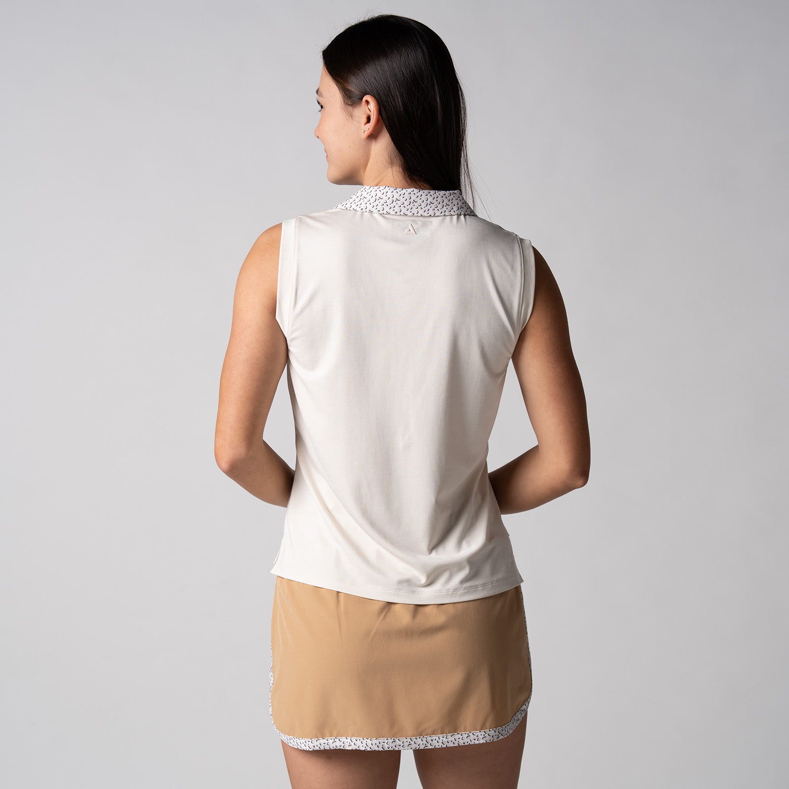 Gray background, female model wearing a JOOLA women's club sleeveless polo, sandstone color.