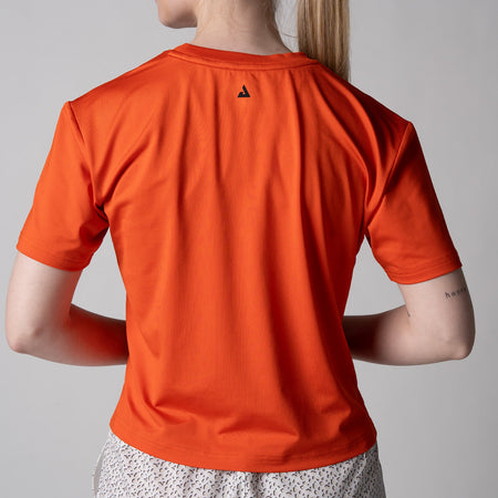 Gray background, close up on the back of a female model wearing a JOOLA women's court crop tee, poppy red color.