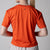 Gray background, close up on the back of a female model wearing a JOOLA women's court crop tee, poppy red color.