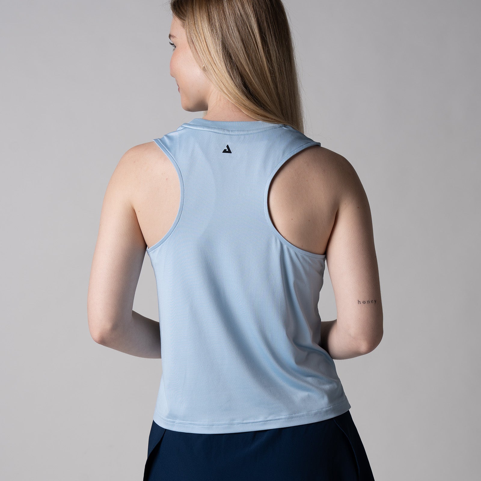 Gray background, image of the back of a female model wearing a JOOLA women's court tank, blue breeze color.