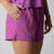 Gray background, close up of a female models hand in the pocket of a pair of JOOLA women's court woven shorts passion purple.