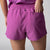 Gray background, close up image of the zipper pocket on the back of a pair of JOOLA women's court woven shorts, passion purple.