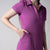 Gray background, image of a female model with her hand in the pocket of a JOOLA women's novelty polo dress, passion purple.