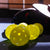 Close up image of five JOOLA HC-40 pickleballs with some paddles in the background.