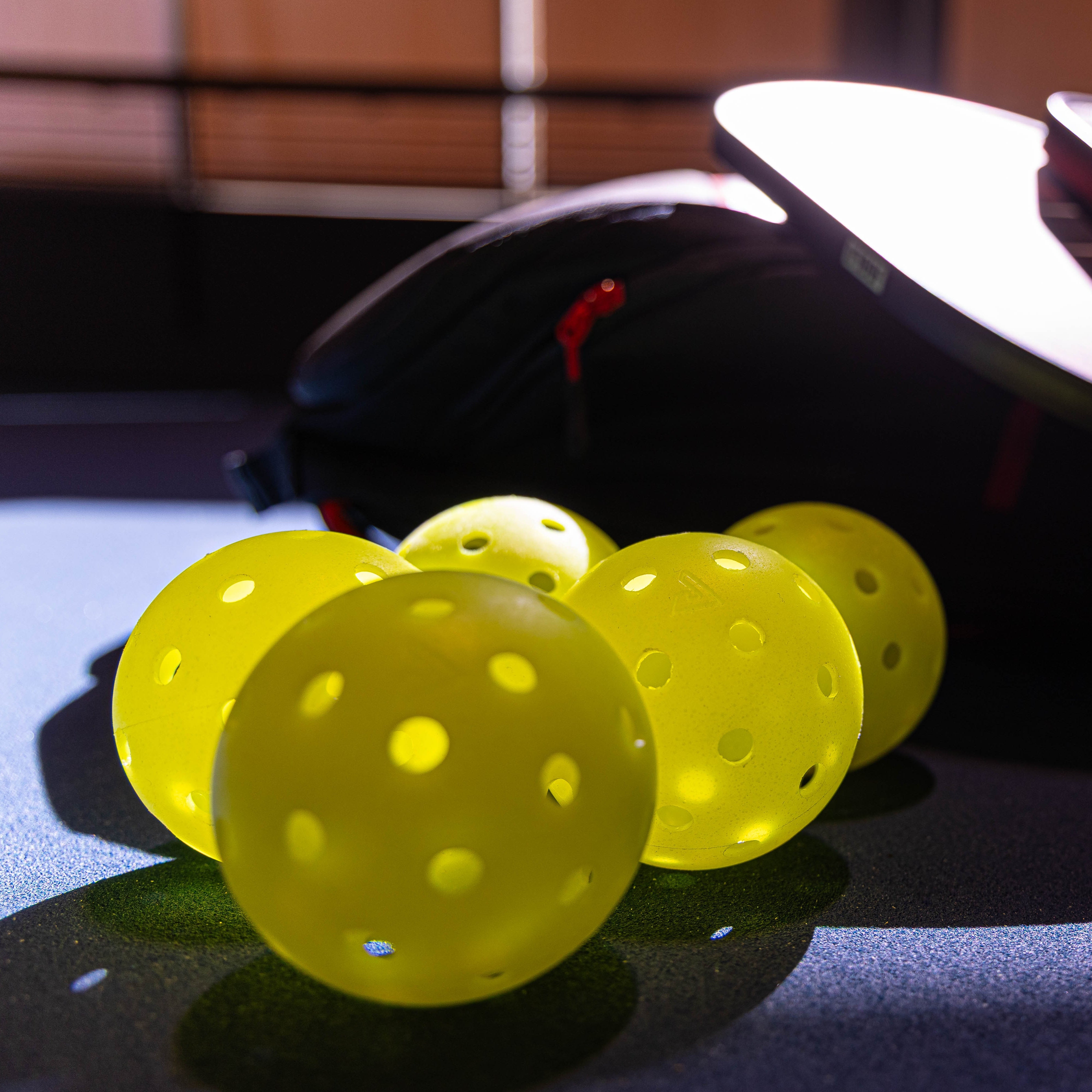 Close up image of five JOOLA HC-40 pickleballs with some paddles in the background.