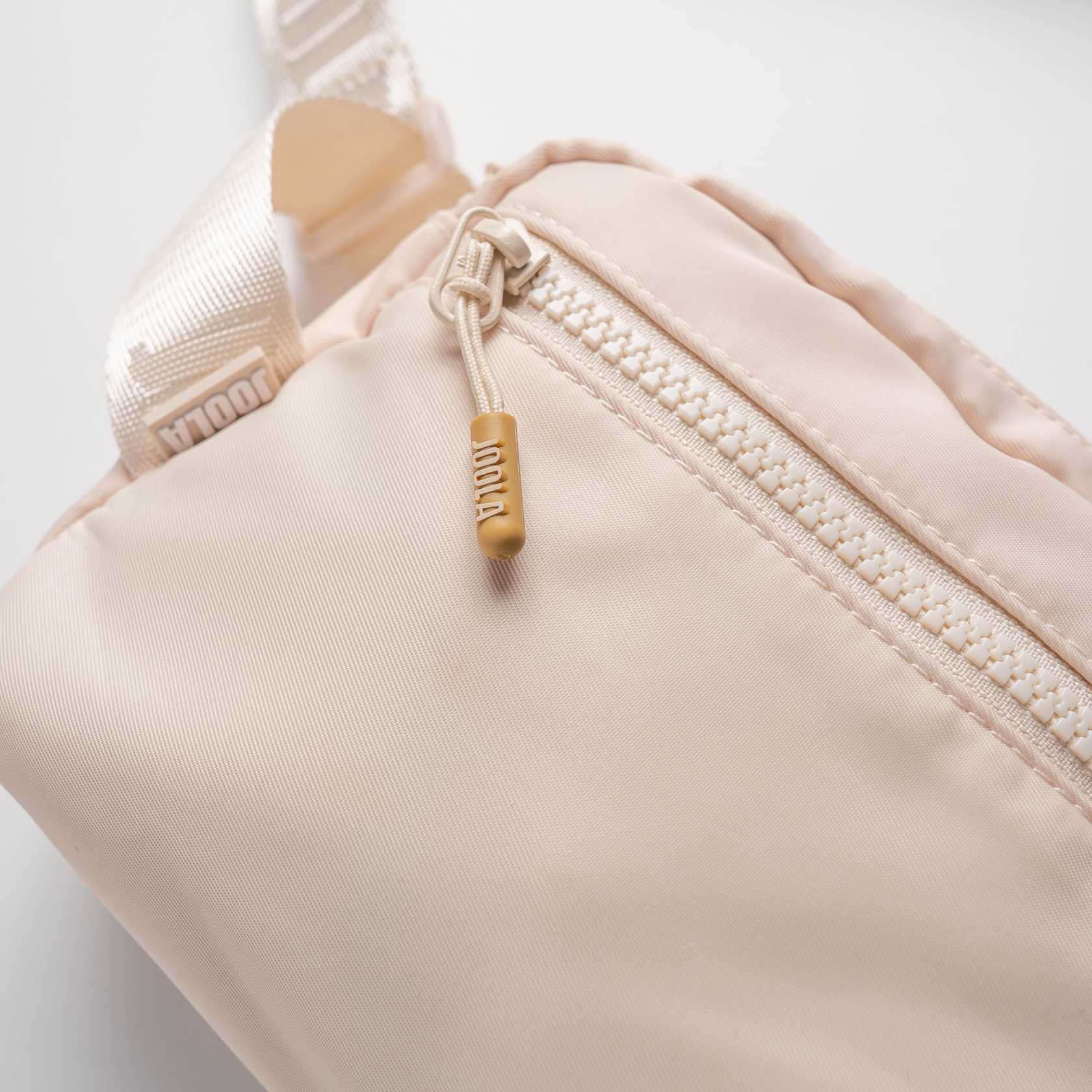 Close up on the JOOLA logo detail on the zipper of a JOOLA Belt Bag, Sandstone color.