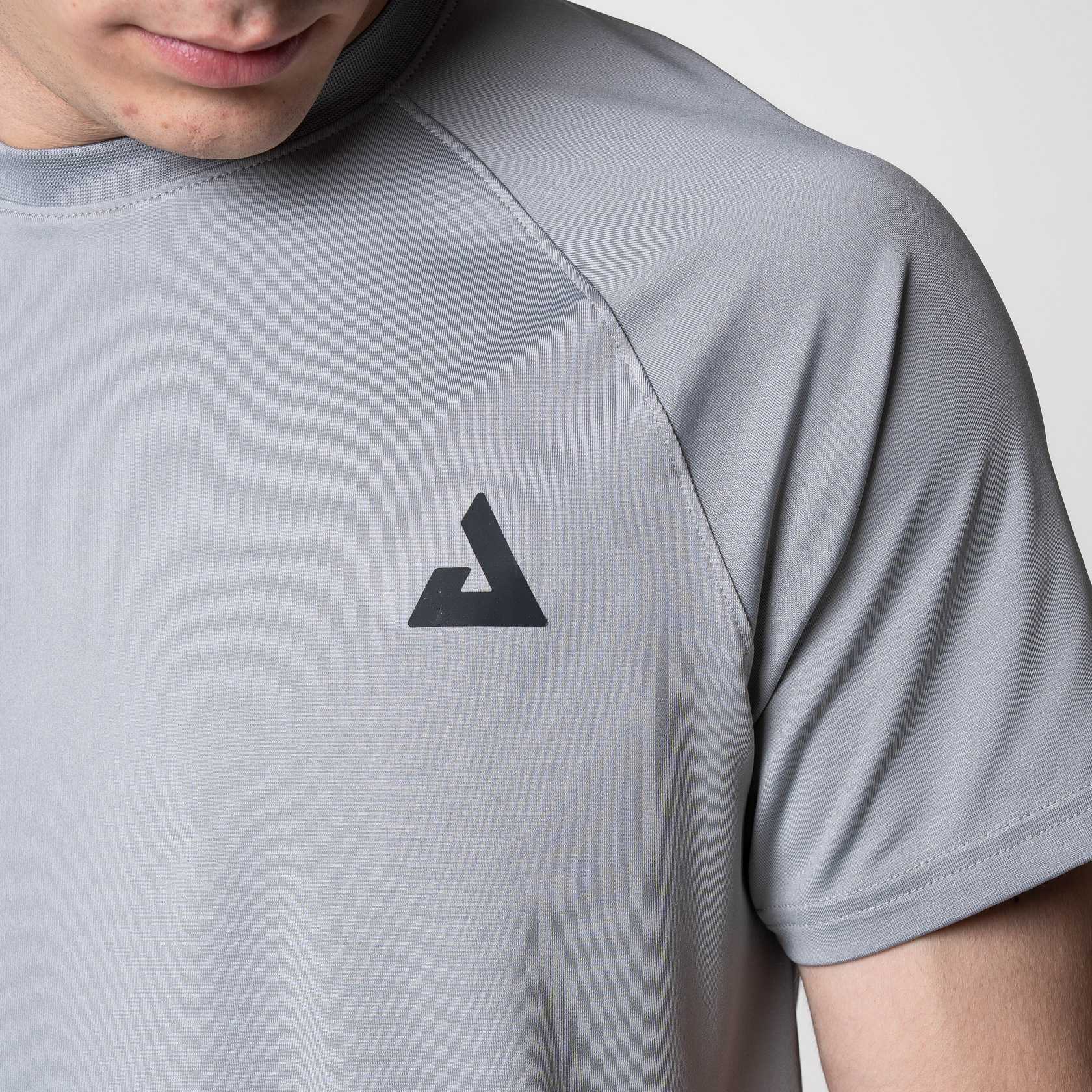 Close up on the black JOOLA trinity logo on the JOOLA Court Short Sleeve Shirt, Gray.