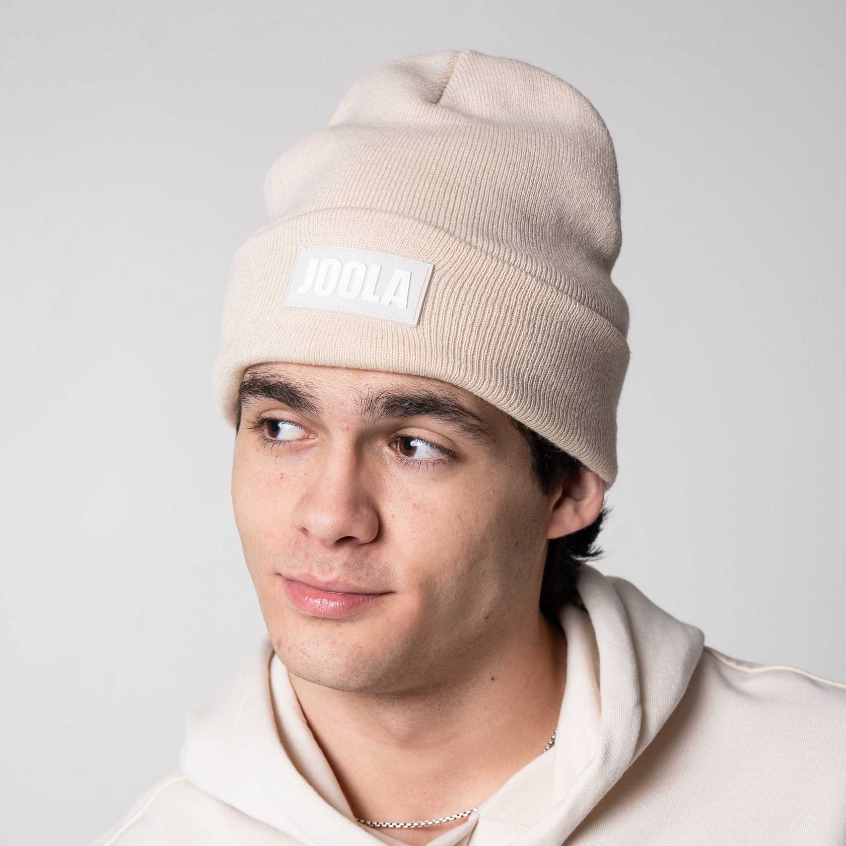 Gray background, image of a male model wearing a JOOLA Cuff Beanie, sandstorm.