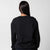 Gray background, image of the back of a female model who is wearing a black fleece crew.