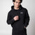 Gray background, image of a male model wearing a black JOOLA Fleece Hoodie.