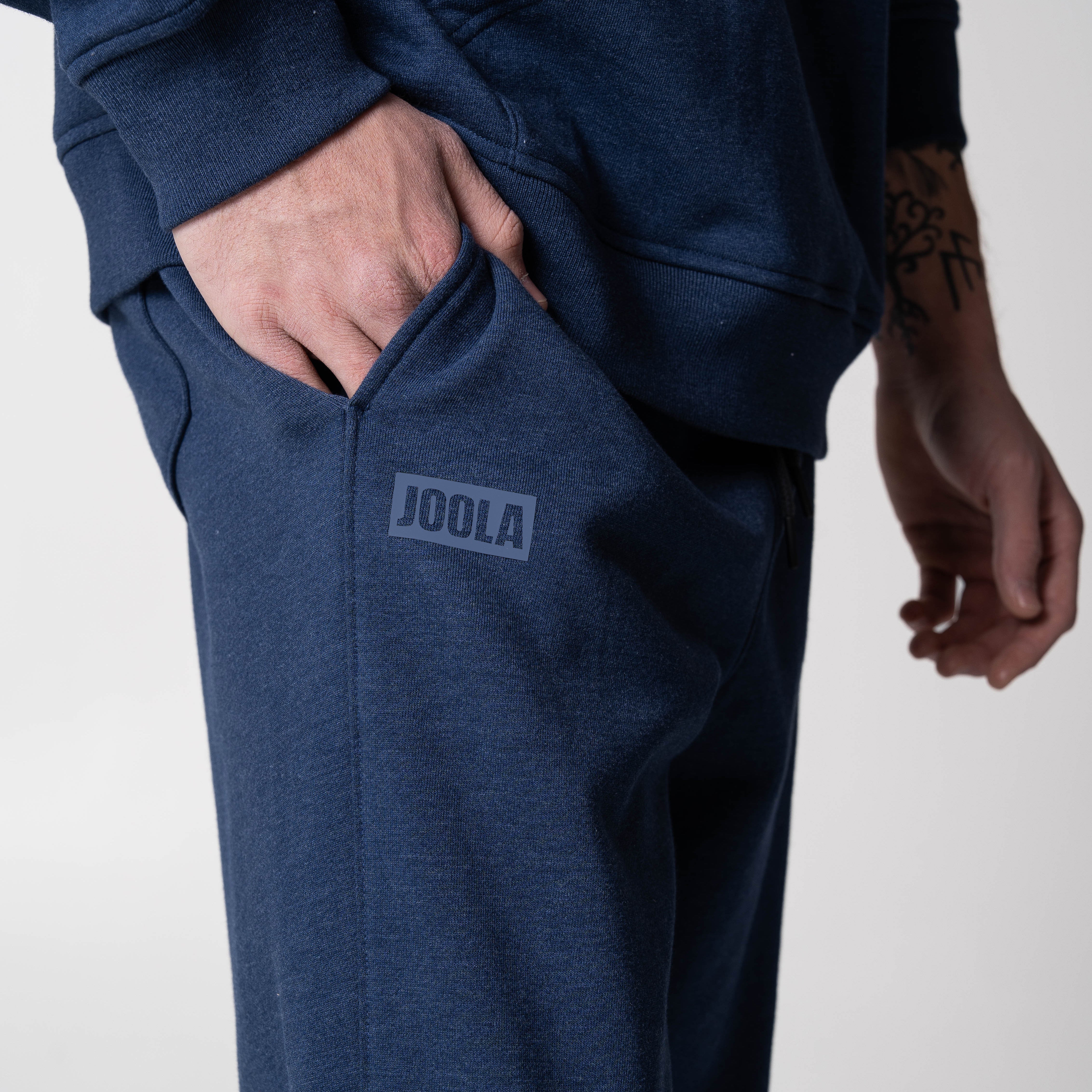Gray background, close up on the JOOLA Wordmark Logo near the pocket on a pair of JOOLA fleece pants (Navy).