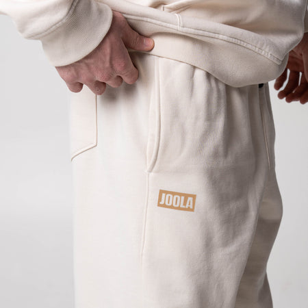 Close up on the JOOLA wordmark logo and pocket detail on a pair of JOOLA Fleece pants (Sandstone).