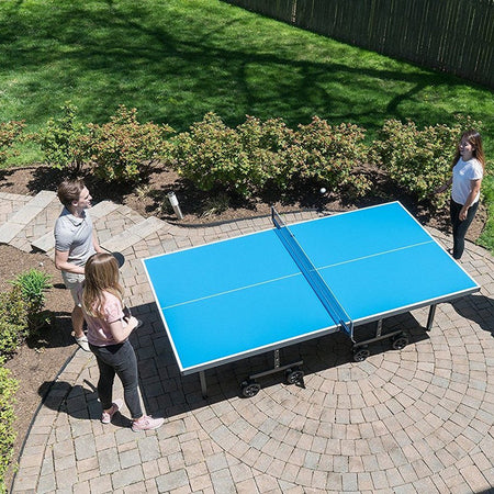 People playing ping pong on an outdoor table in a backyard setting.