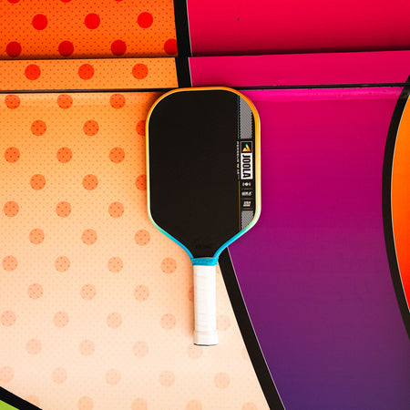 JOOLA Perseus Summer Daze Pickleball paddle with black surface, orange, blue, green and yellow color gradient on the rim, and white handle on a colorful background.