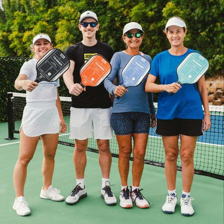 Four people on a tennis court holding pickleball paddles.