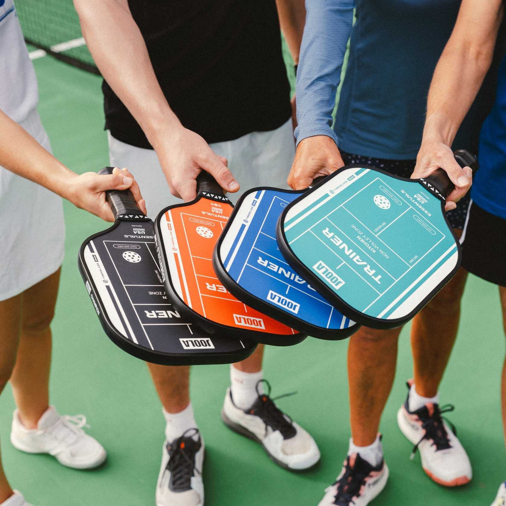 Four people holding colorful pickleball paddles on a pickleball court.